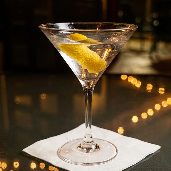 Martini with a lemon twist on a white napkin, with blurred lights in the background.
