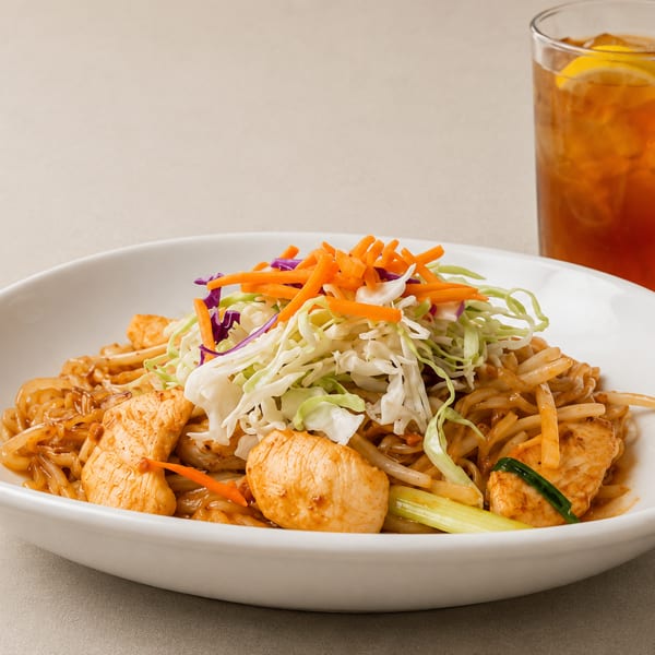 Chicken Pad Thai with shredded cabbage, carrots, and a glass of iced tea.