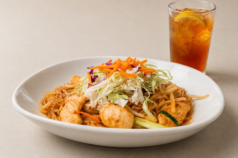 Chicken Pad Thai with shredded cabbage, carrots, and a glass of iced tea.