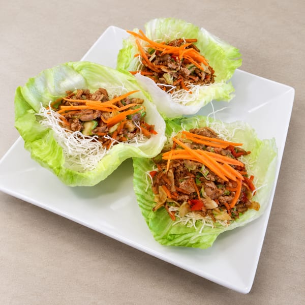Three lettuce wraps filled with meat, shredded carrots, and crispy noodles on a white plate.