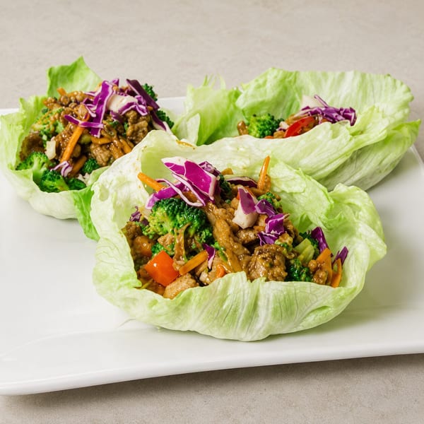 Three vibrant lettuce wraps filled with stir-fried meat, broccoli, carrots, and red cabbage.