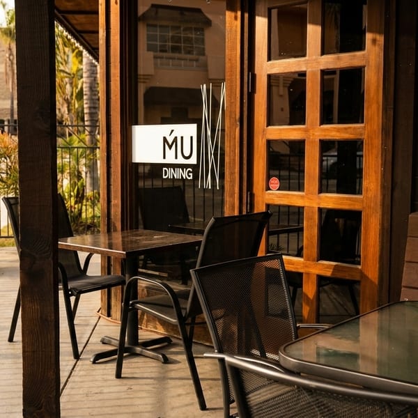Outdoor patio of MU Dining with tables, chairs, and a wooden door with a sign.
