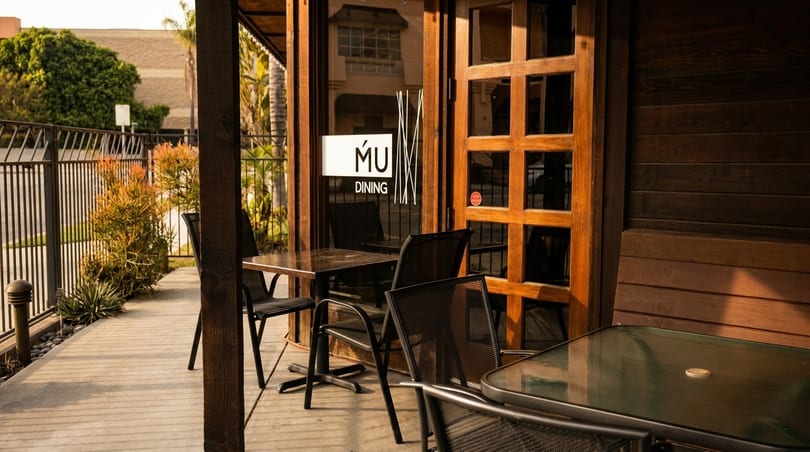 Outdoor patio of MU Dining with tables, chairs, and a wooden door with a sign.