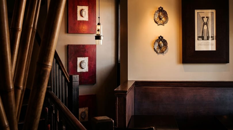 Restaurant interior with bamboo, dark wood railings, red and white art, and wall sconces.