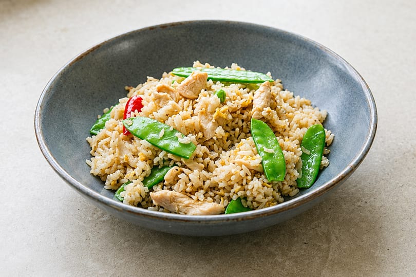 Chicken fried rice with snow peas and red pepper in a gray bowl.