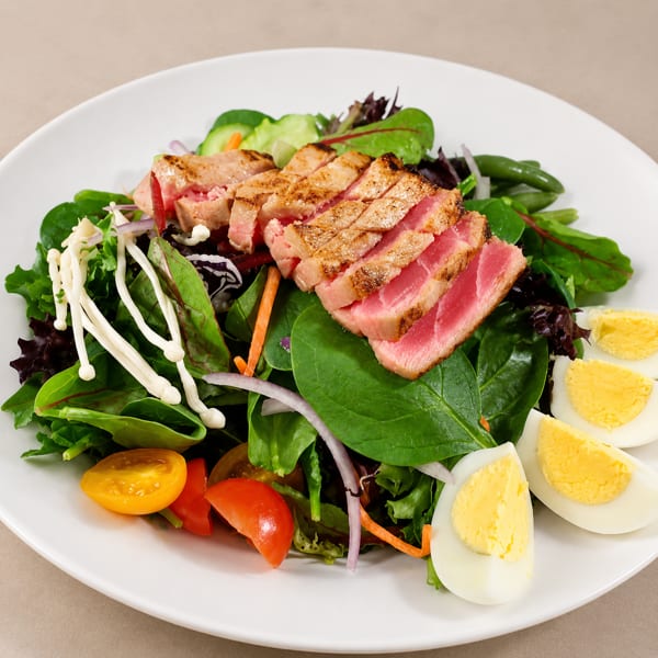 Seared tuna salad with mixed greens, cherry tomatoes, mushrooms, and hard-boiled eggs on a white plate.