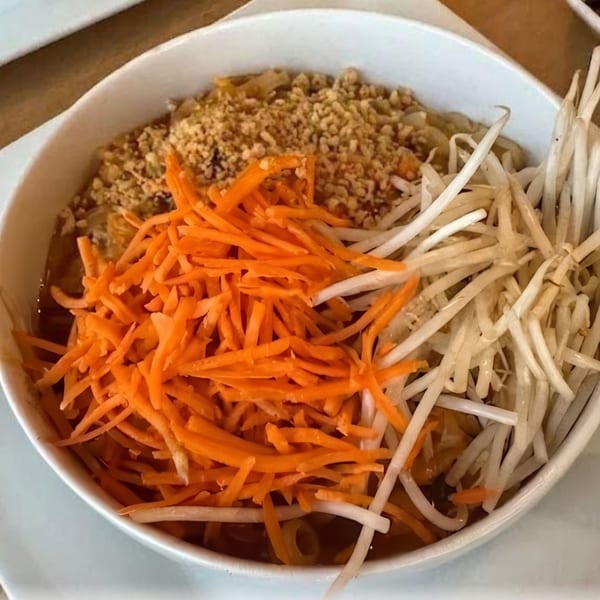 A white bowl of Pad Thai noodles topped with shredded carrots, bean sprouts, and crushed peanuts.